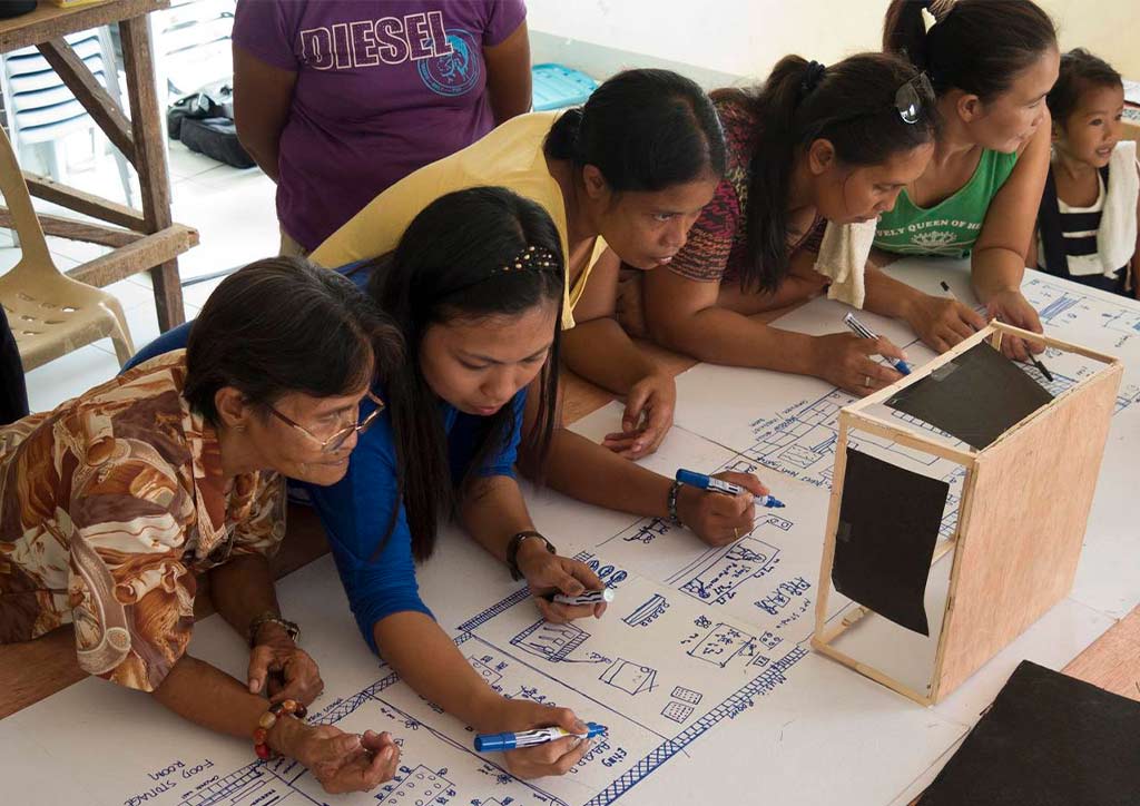 Women from the community draw on a long piece of paper.