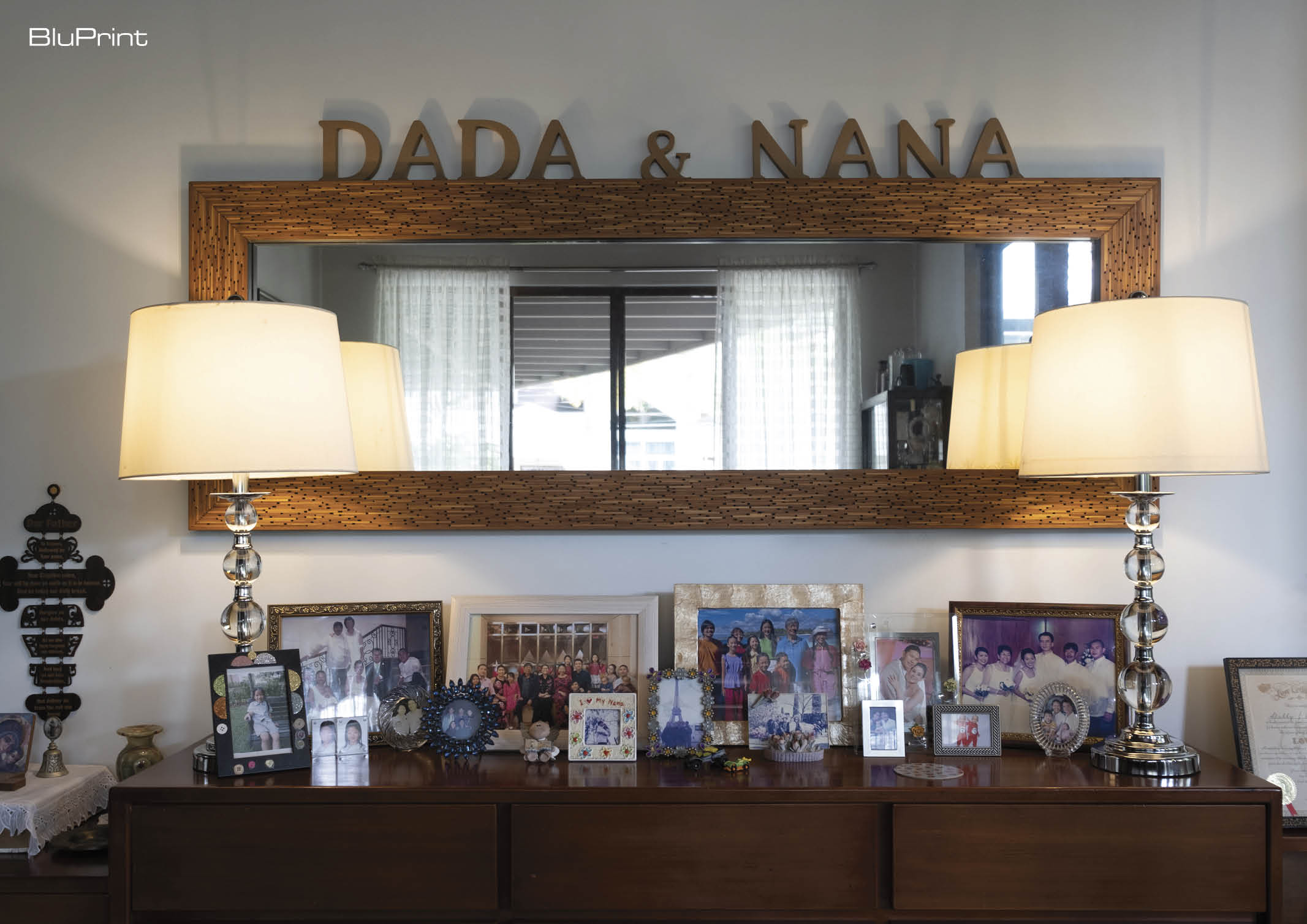 A traditional sideboard with family photographs flanked by table lamps with a long rectangular mirror above it