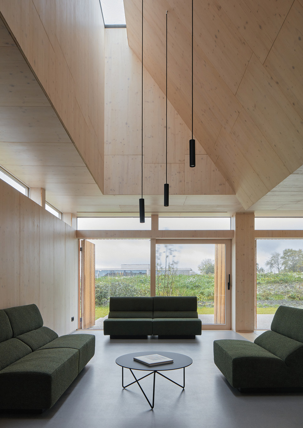 A lounge area with dark green couches next to tall windows inside Warm Nest, a Maggie care facility.