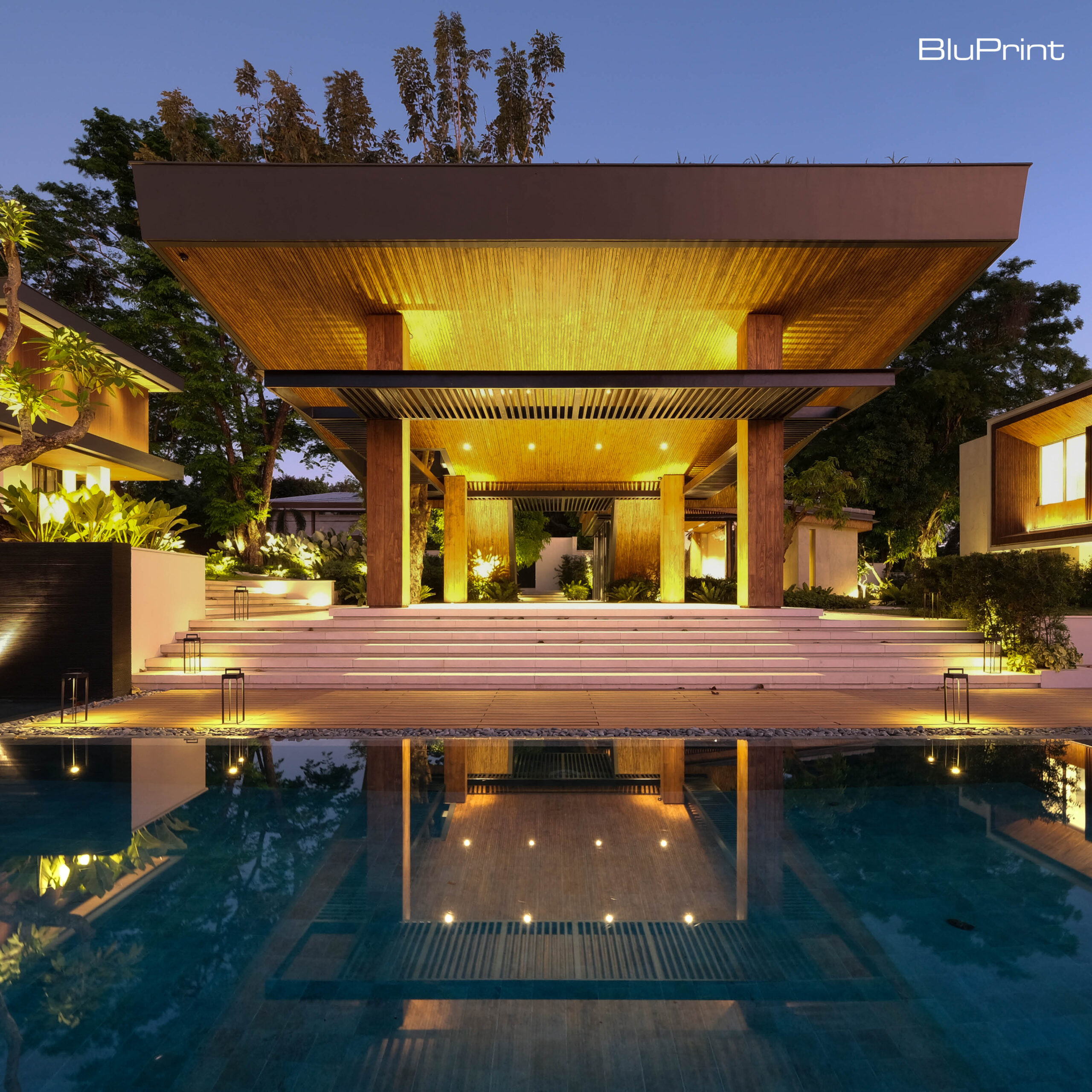 A large pavilion lit up at night with a steps leading toward a swimming pool.