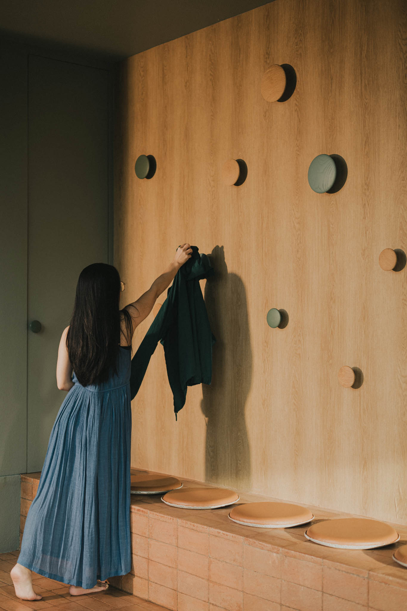 R House's foyer with round wooden pegs for hanging clothes and a brick bench for changing shoes.