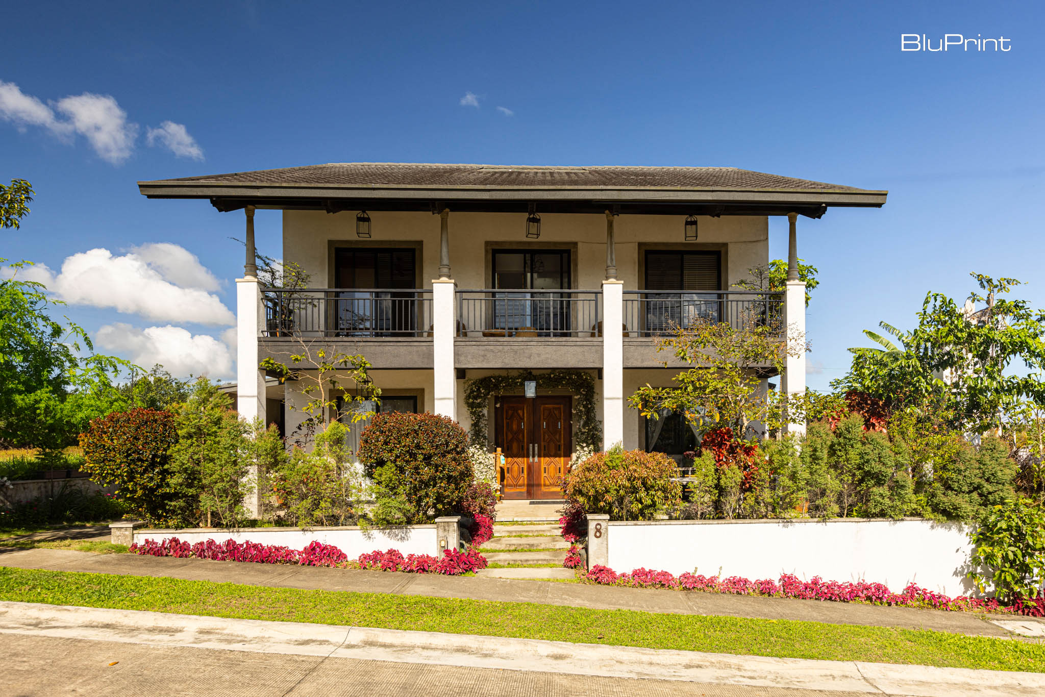 A two storey symmetrical home built on a sloping street with white columns and pitched roof.