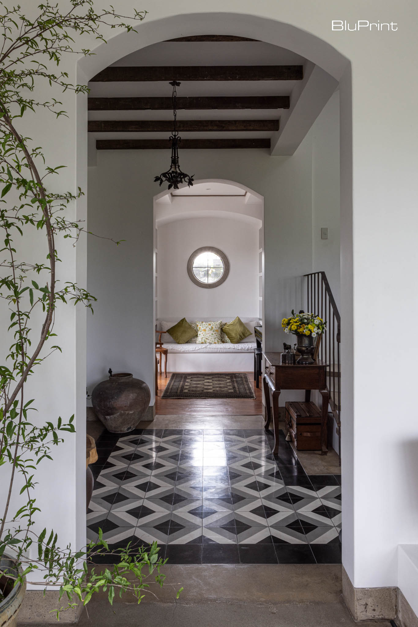 A long arched hallway with patterned tiles leading to a white sofa under a round window.