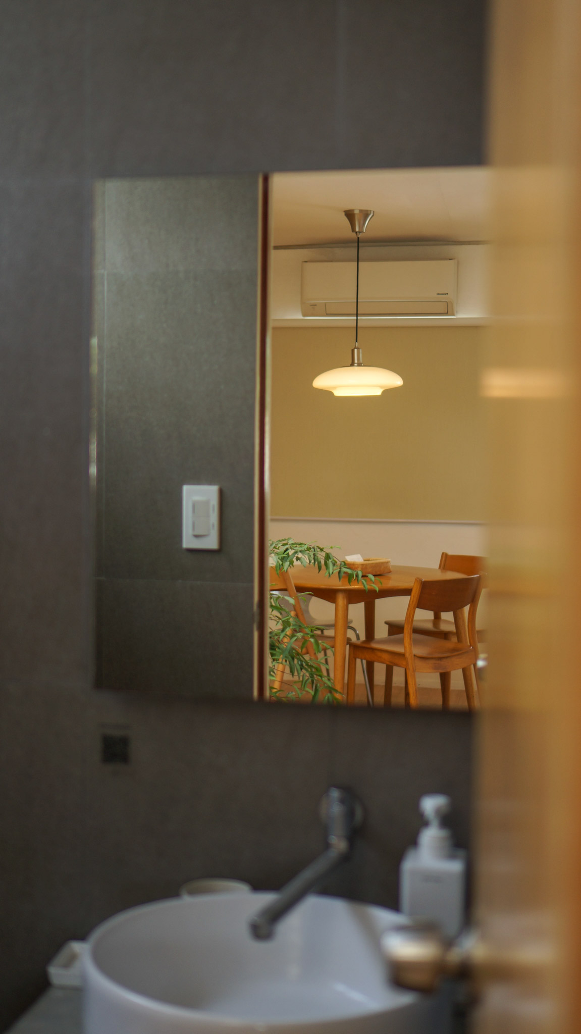 A small white bathroom sink with a mirror above it reflecting the dining room outside. A small house design in San Juan, La Union.