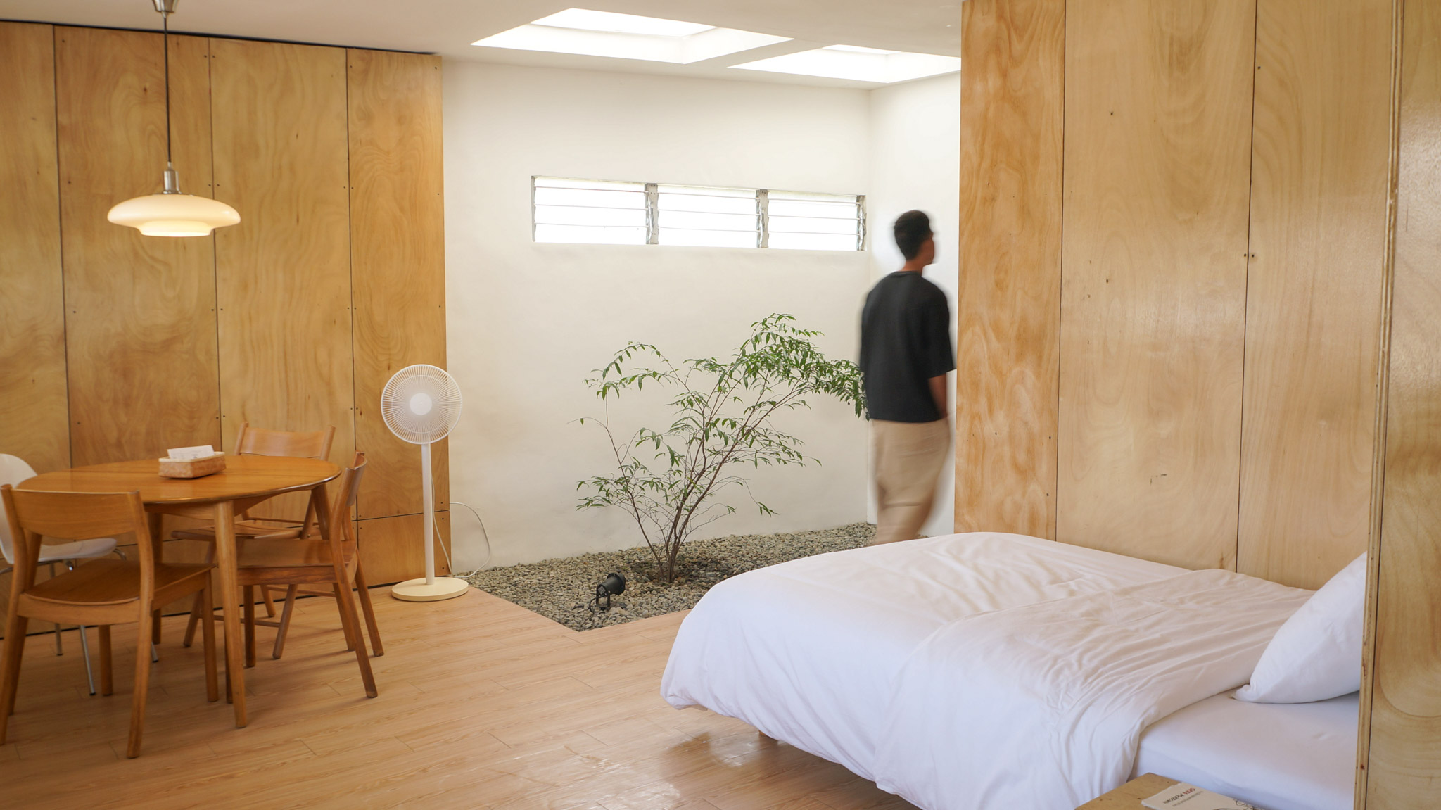 A double bed looking into a small indoor garden with a solitary tree under skylights,