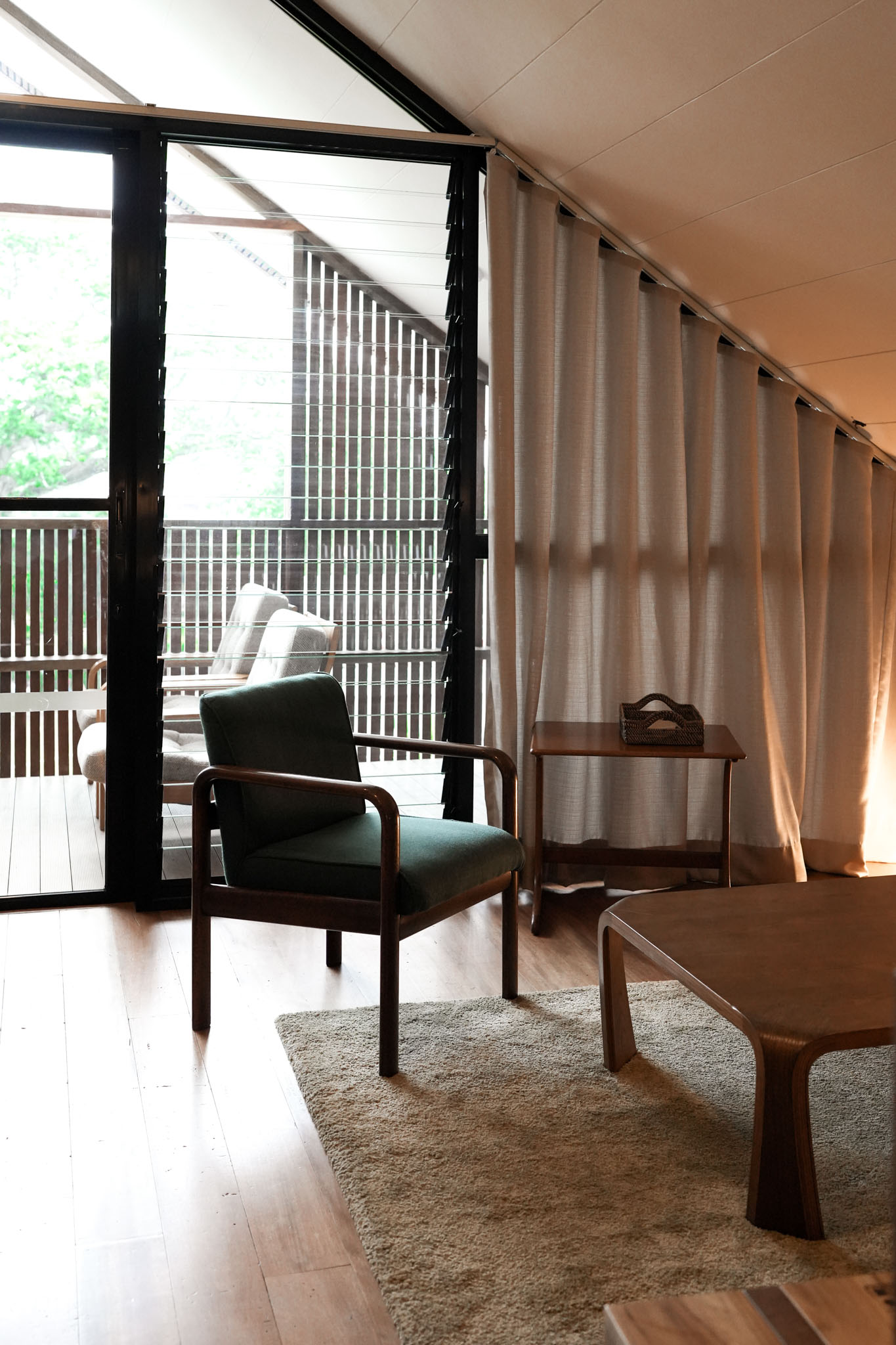 A small living area at the Lark in San Juan La union, with a wooden arm chair and coffee table under a pitched ceiling. The window looks out to an outdoor seating area.