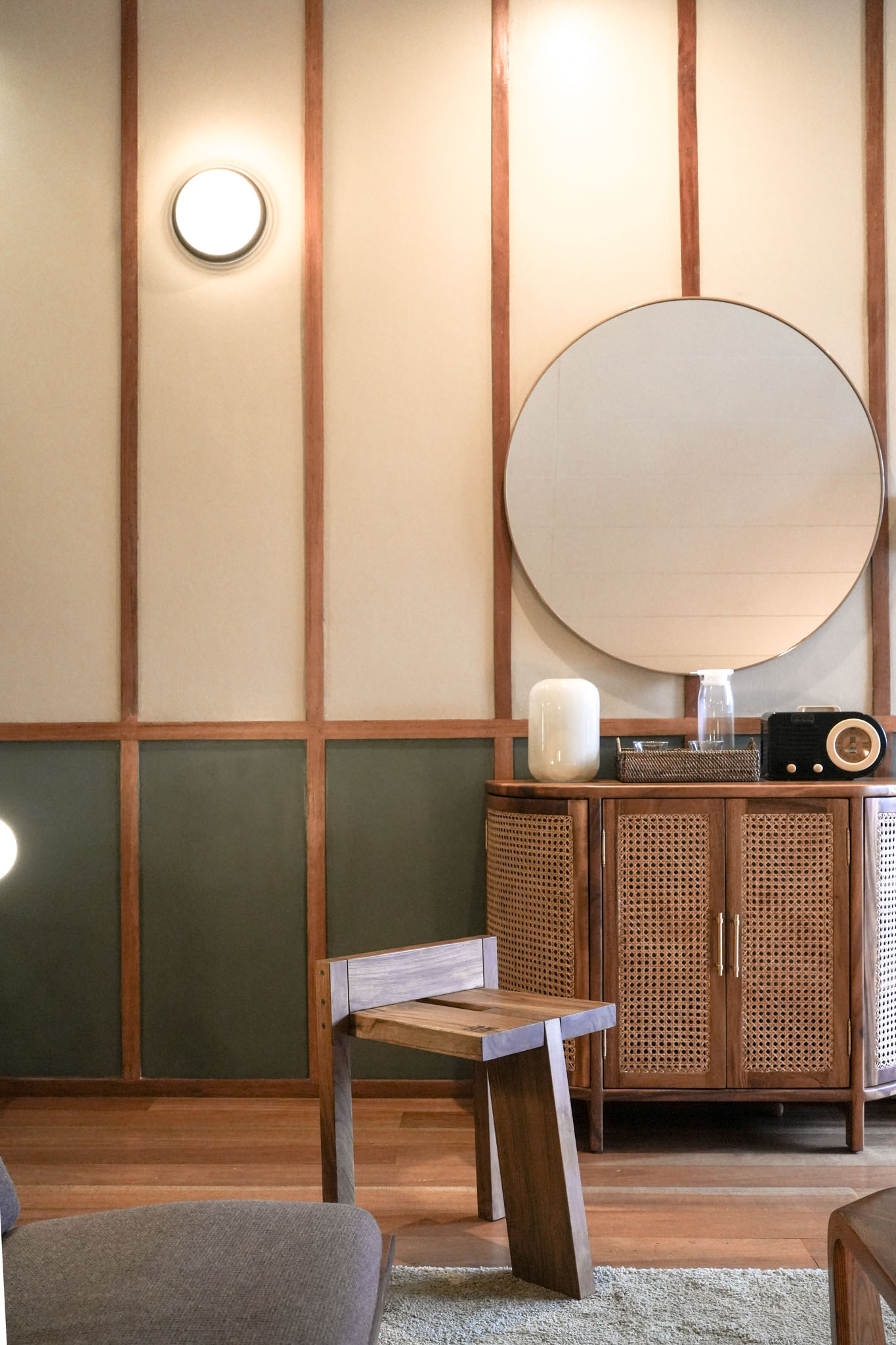 A living area in the Lark located in San Juan, La Union, with a small vanity and woven doors, a round mirror above it, and round sconce. There's a small wooden stool and a chair.