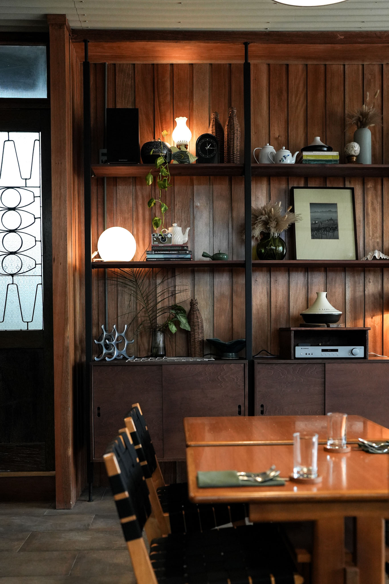 The dining area, with wooden tables and chairs, and a large shelving unit filled with curios and art work.