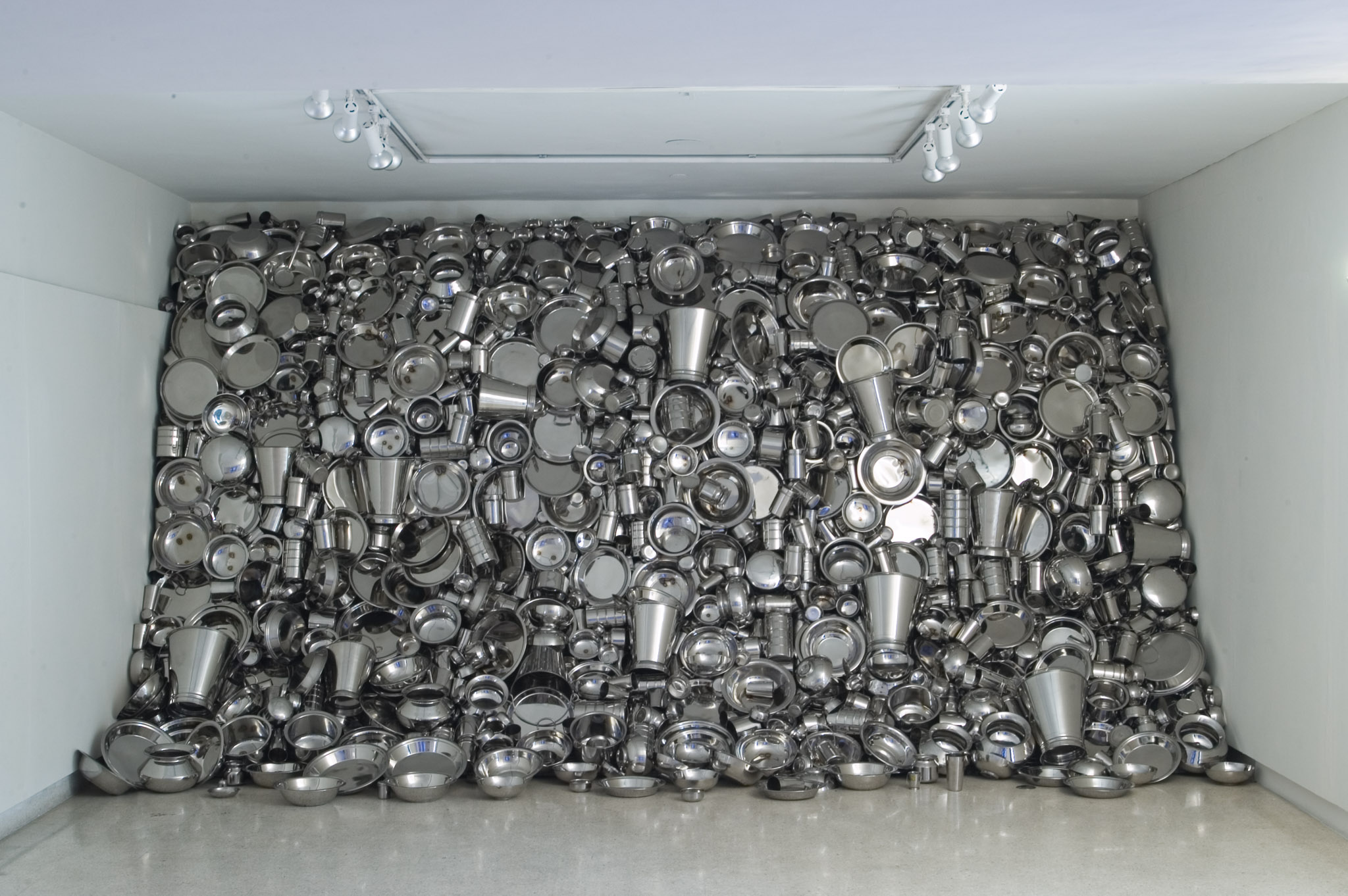 Installation art made of metal pots, pans, and containers occupying an entire wall.
