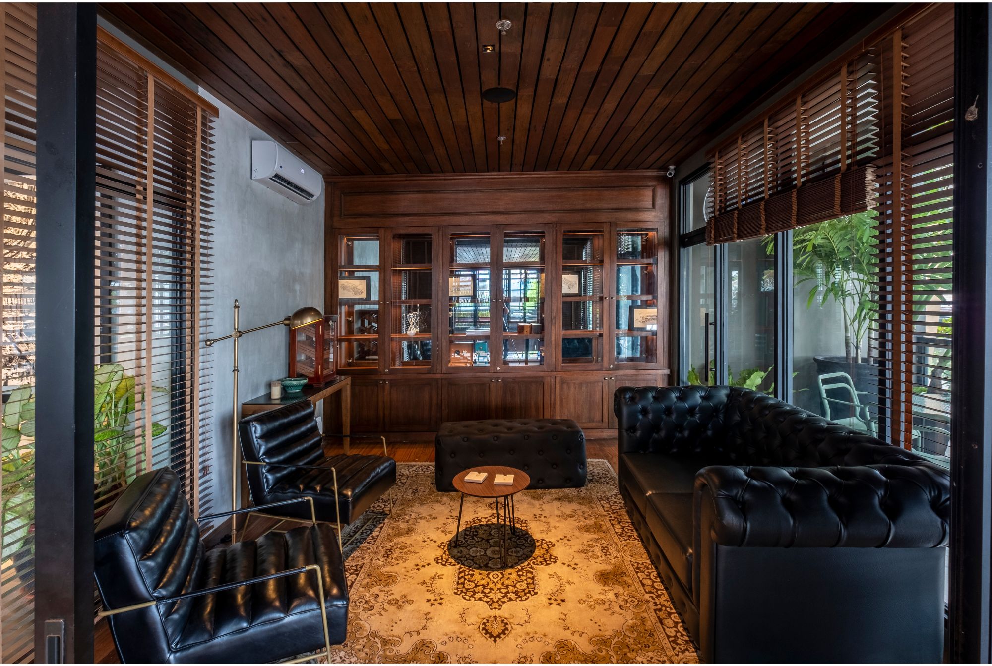 A cigar room with leather chesterfield sofa, matching armchairs, and a wooden built in displaying cigars.