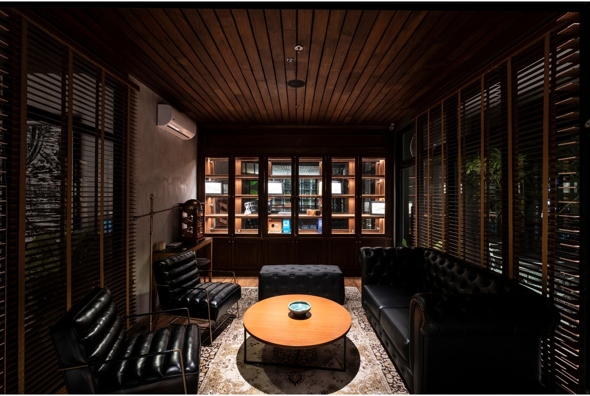 A cigar room with leather chesterfield sofa, matching armchairs, and a wooden built in displaying cigars.