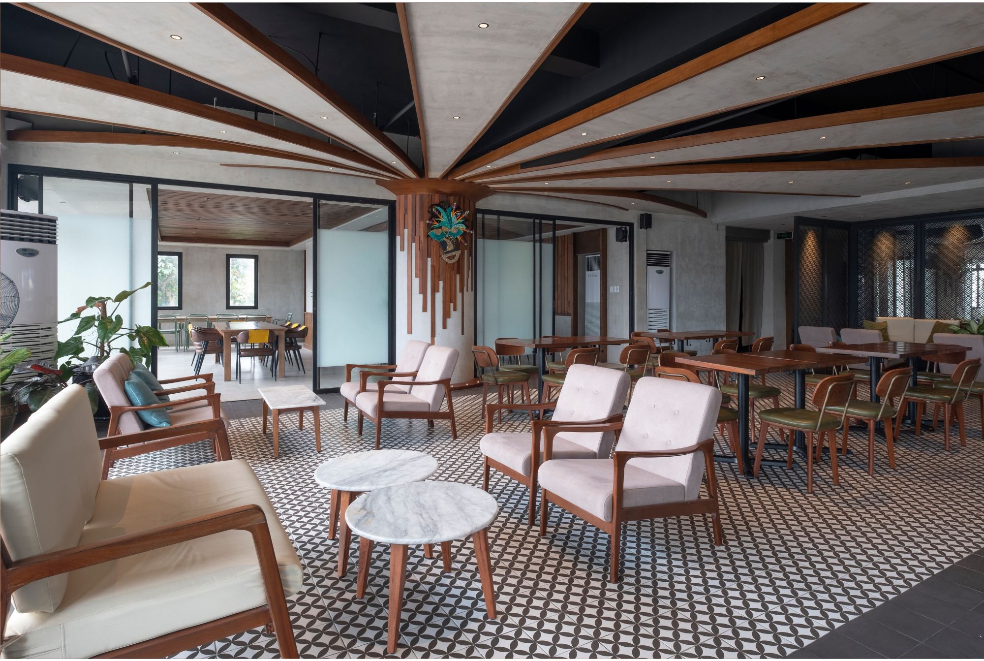 A dining area with tables, seating, and a lounge area with an architectural ceiling treatement.