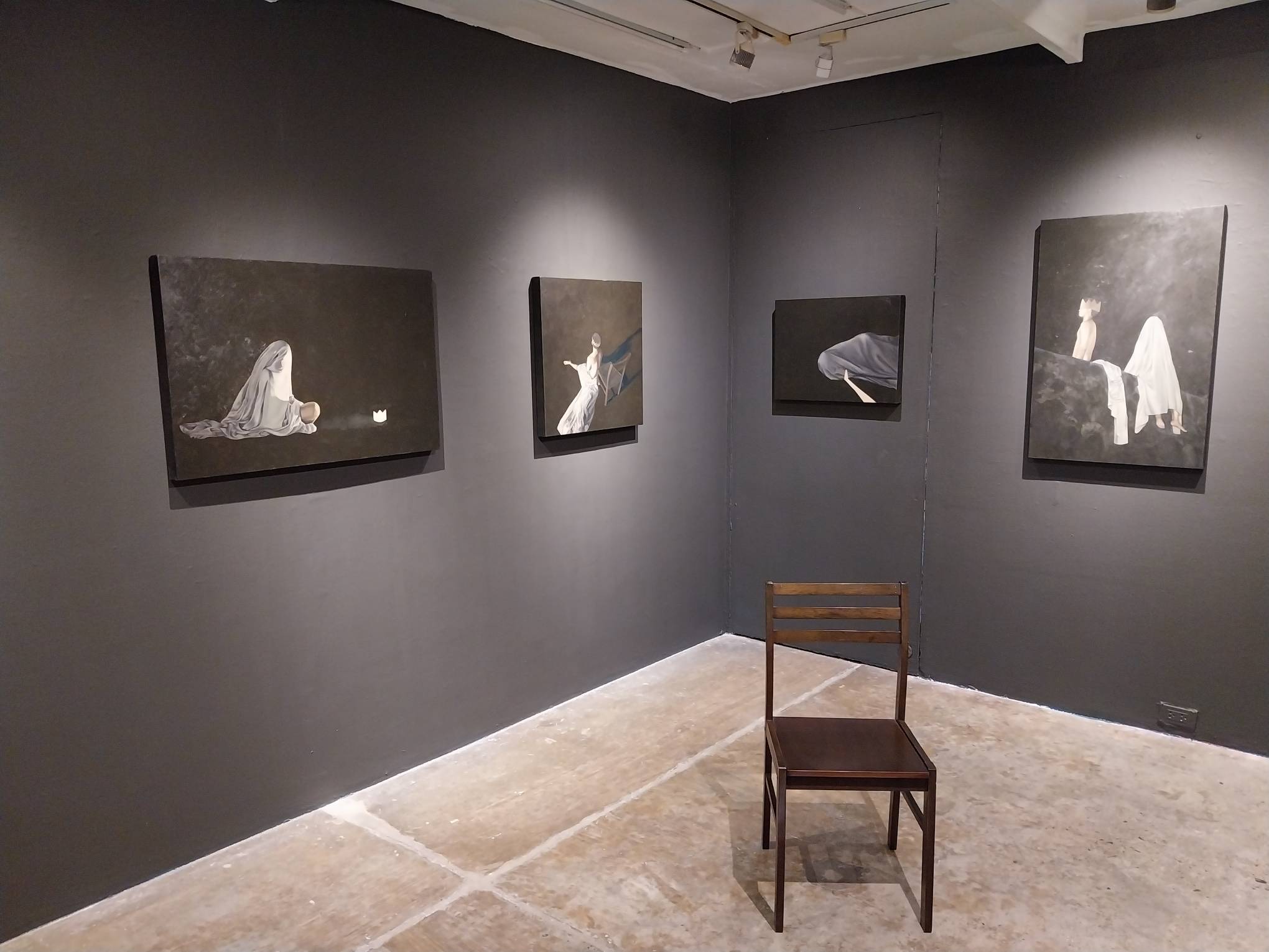 Some of the paintings for Gelo Montiero's new exhibit, with a wooden chair in the center. Photo by Elle Yap.