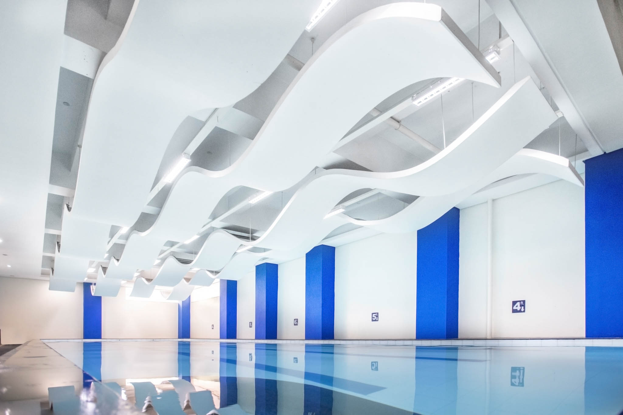 The pool area features waveform ceiling ornaments that echo the maritime theme, enhancing the sports center’s cohesive design.