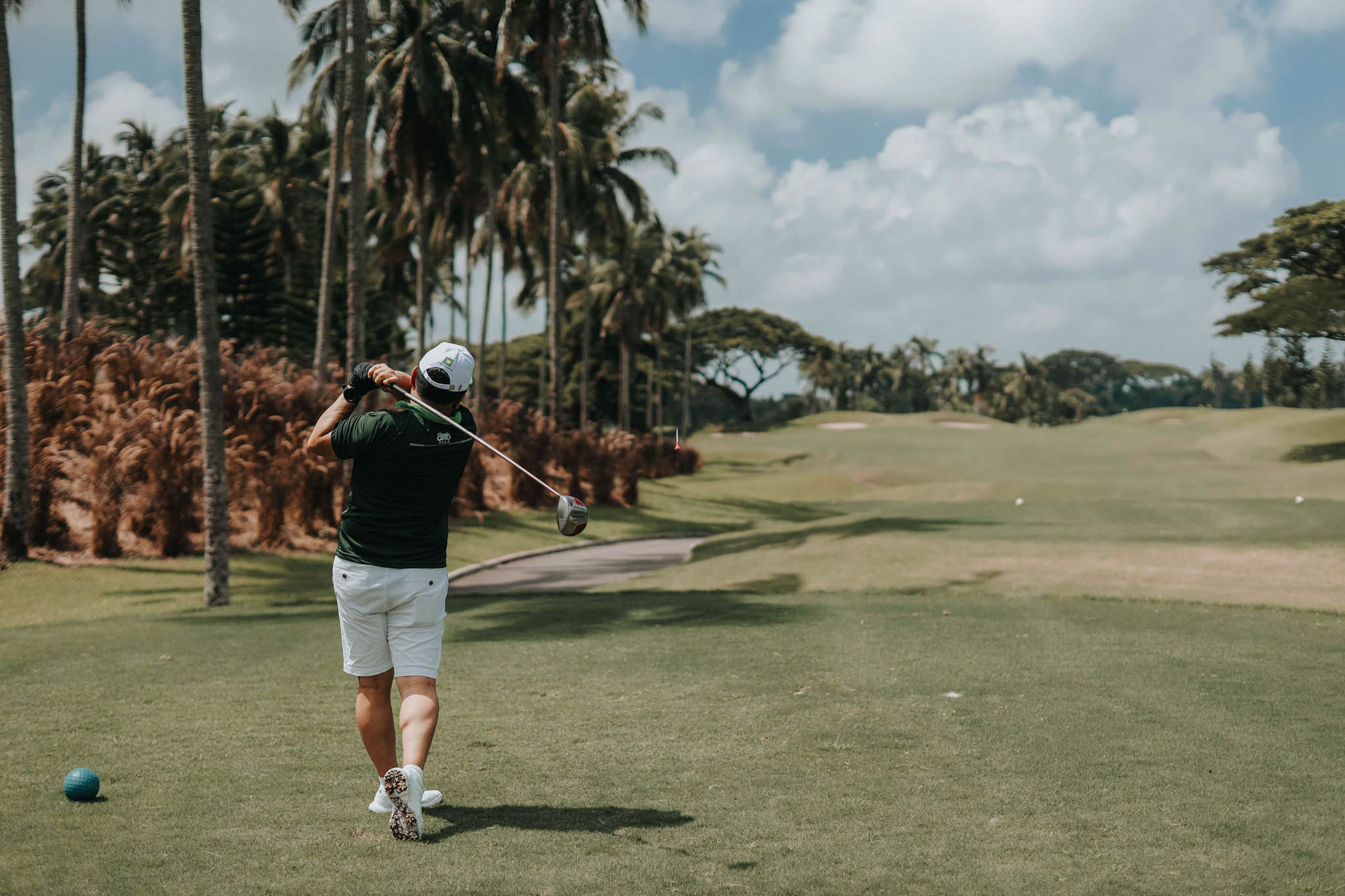 A participant in a golf tournament swinging his golf club at a golf course.