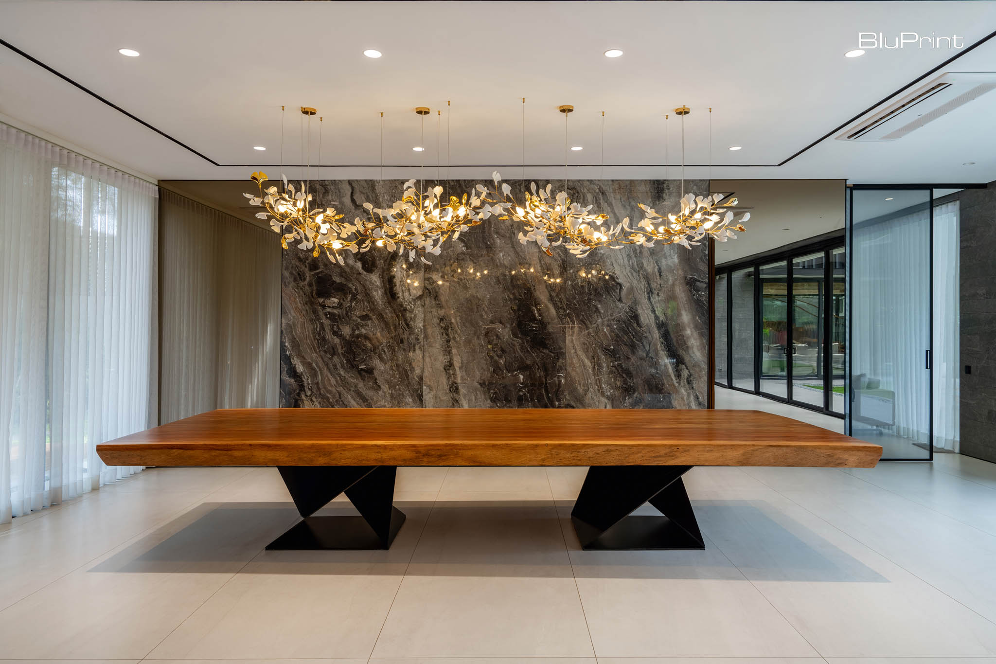 S Residence: Shelter in Place by Sim Ateliers. Designed for entertaining, the home’s stunning dining room elevates every gathering with its grand wooden table, marble accent wall, and sculptural chandelier.