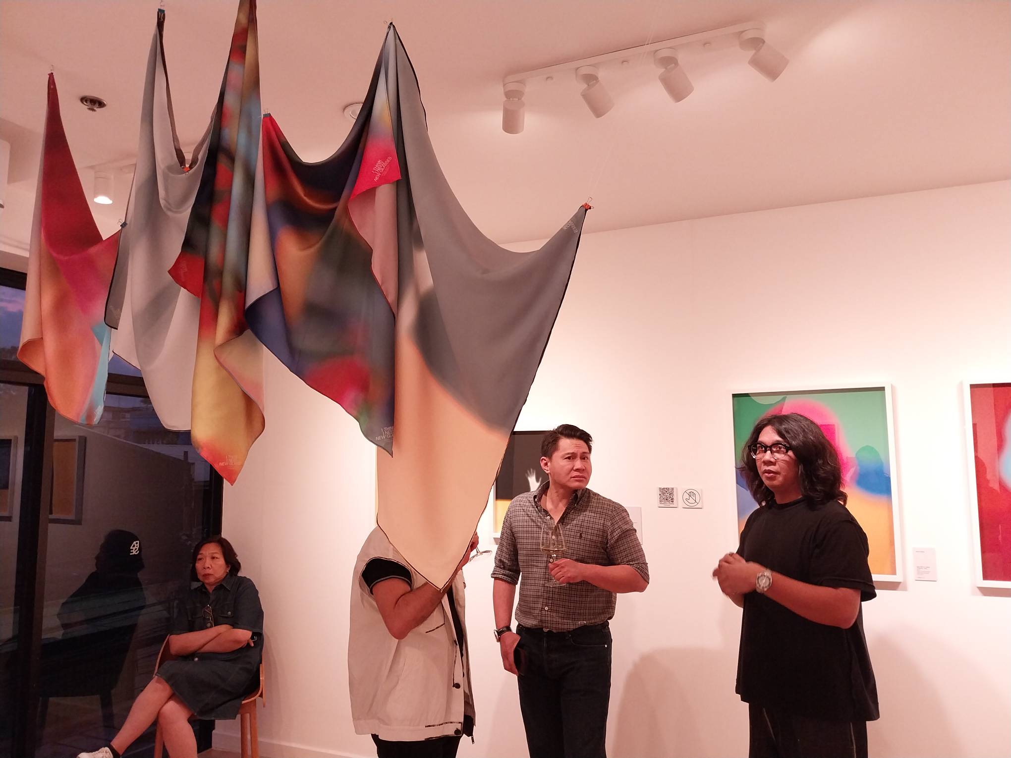 The artist [far right] explaining the hanging fabric prints for "I Think I Need New Glasses."