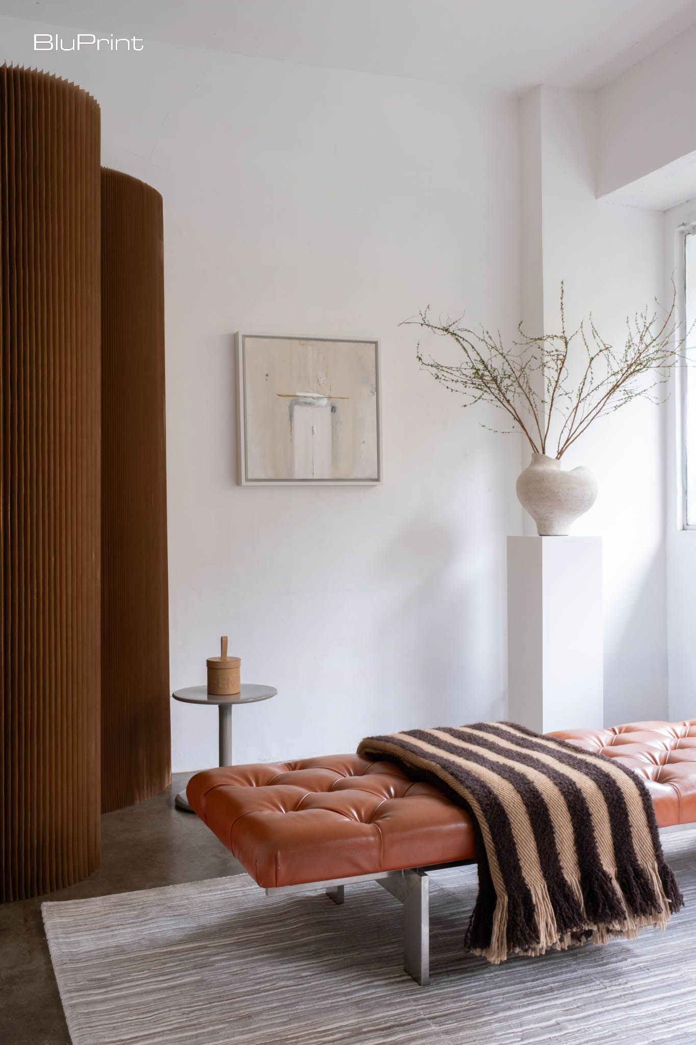A mocha mousse vignette showing a daybed with a throw on it, a vase on a pedestal, and a divider.