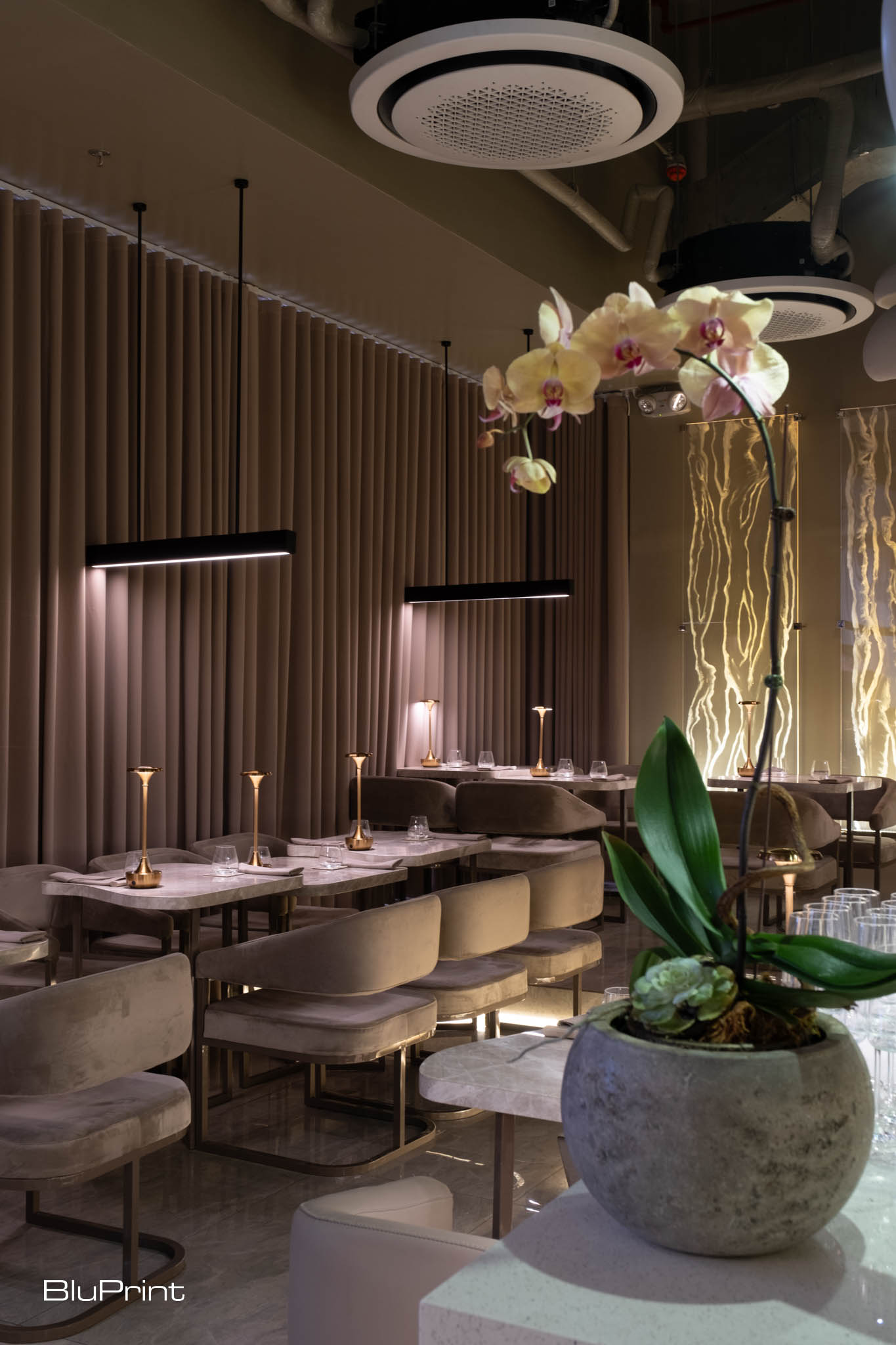 Interiors of Taupe restaurant featuring marble tables, upholstered chairs, and gray curtains.