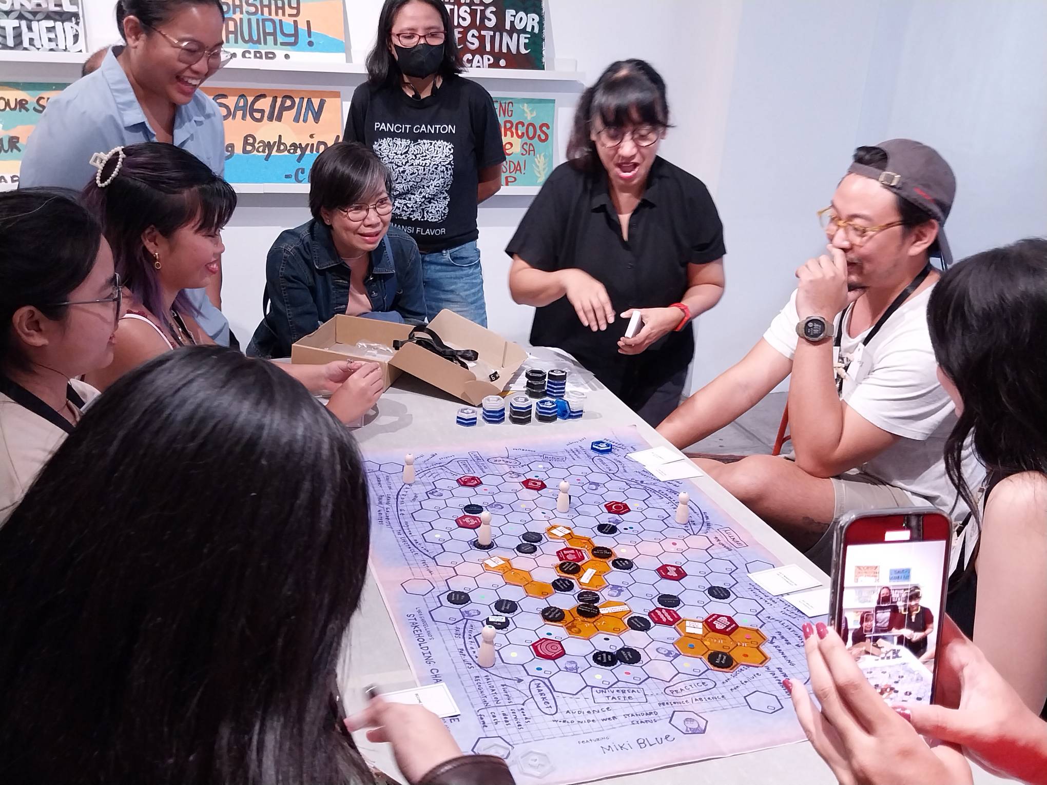 Lyra Garcellano explaining the rules of "Stakeholding" as the players run through the board game.