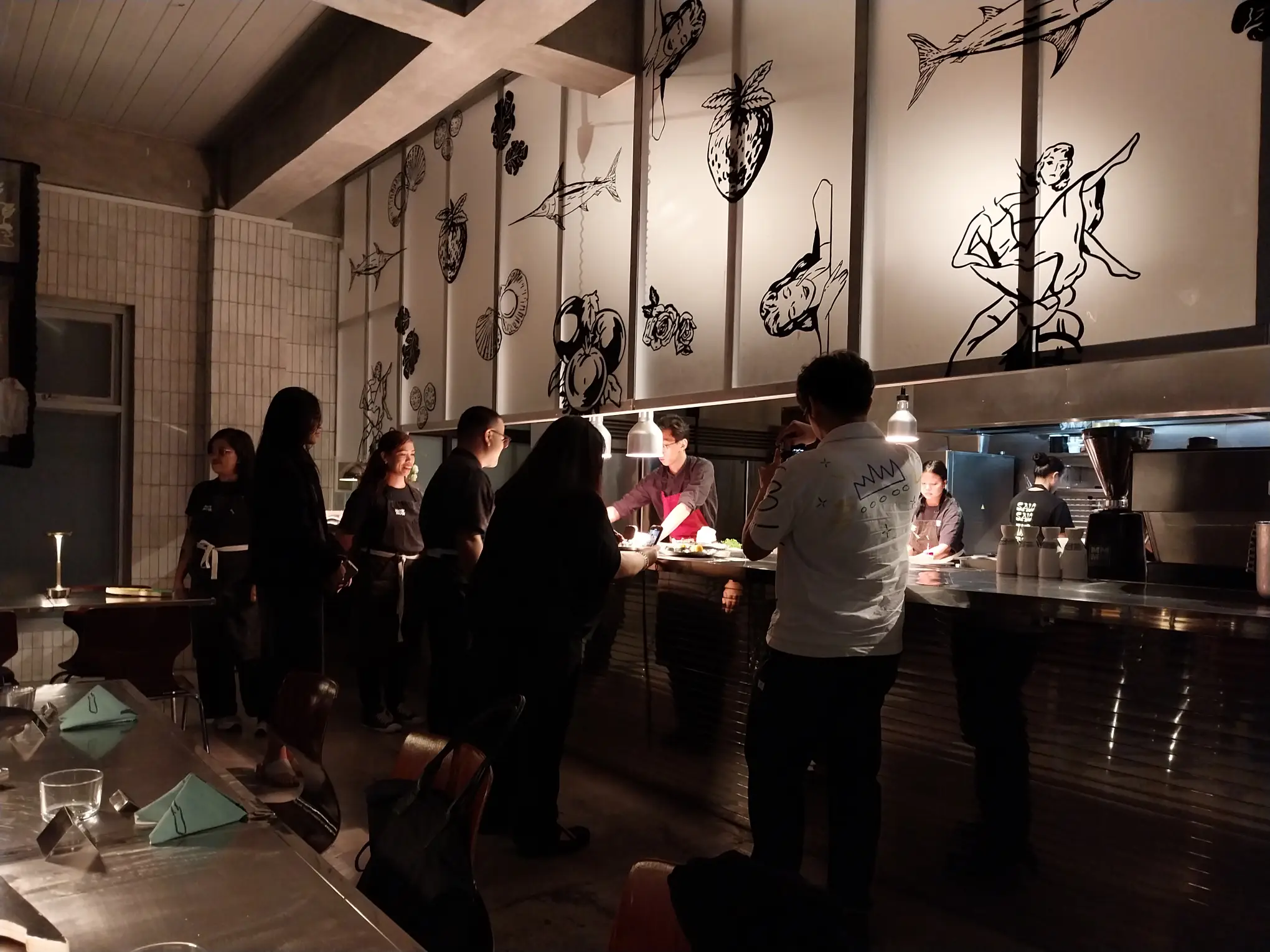 'reNOWn x Isabel Reyes Santos' with people watching the cooking in the kitchen.