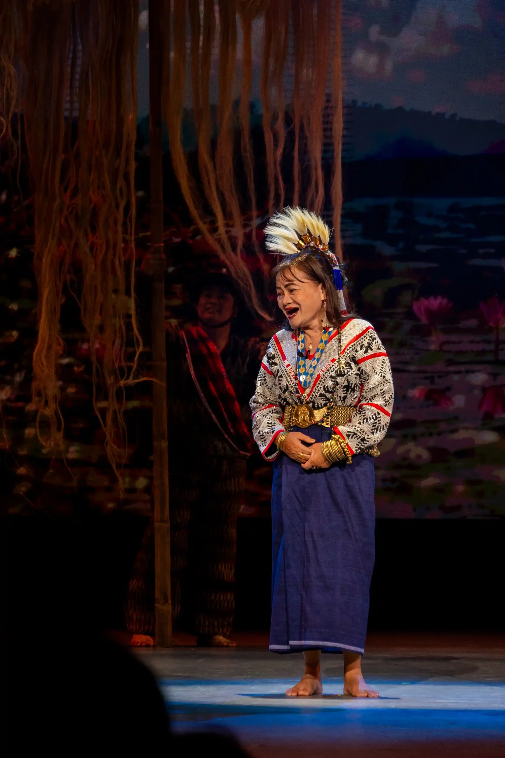 Rosie Godwino Sula, National Living Treasure and chanter of the T'boli epic Tudbulul, opens the Philippine National Day performance in traditional T'boli ceremonial dress: a layered ensemble of brass, beads, and handwoven cloth including the kgal bensewit blouse, t’deyung ginggung skirt, hilet tenwel brass belt, and slo’ung knibang headdress.