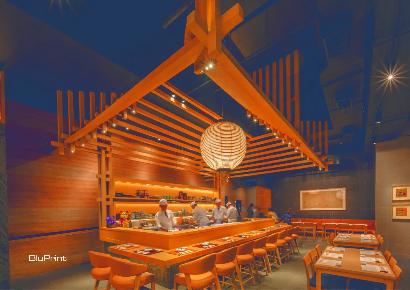 The centrally positioned sushi bar under a striking wooden canopy inspired by traditional Japanese joinery pays homage to time-honored craftsmanship.