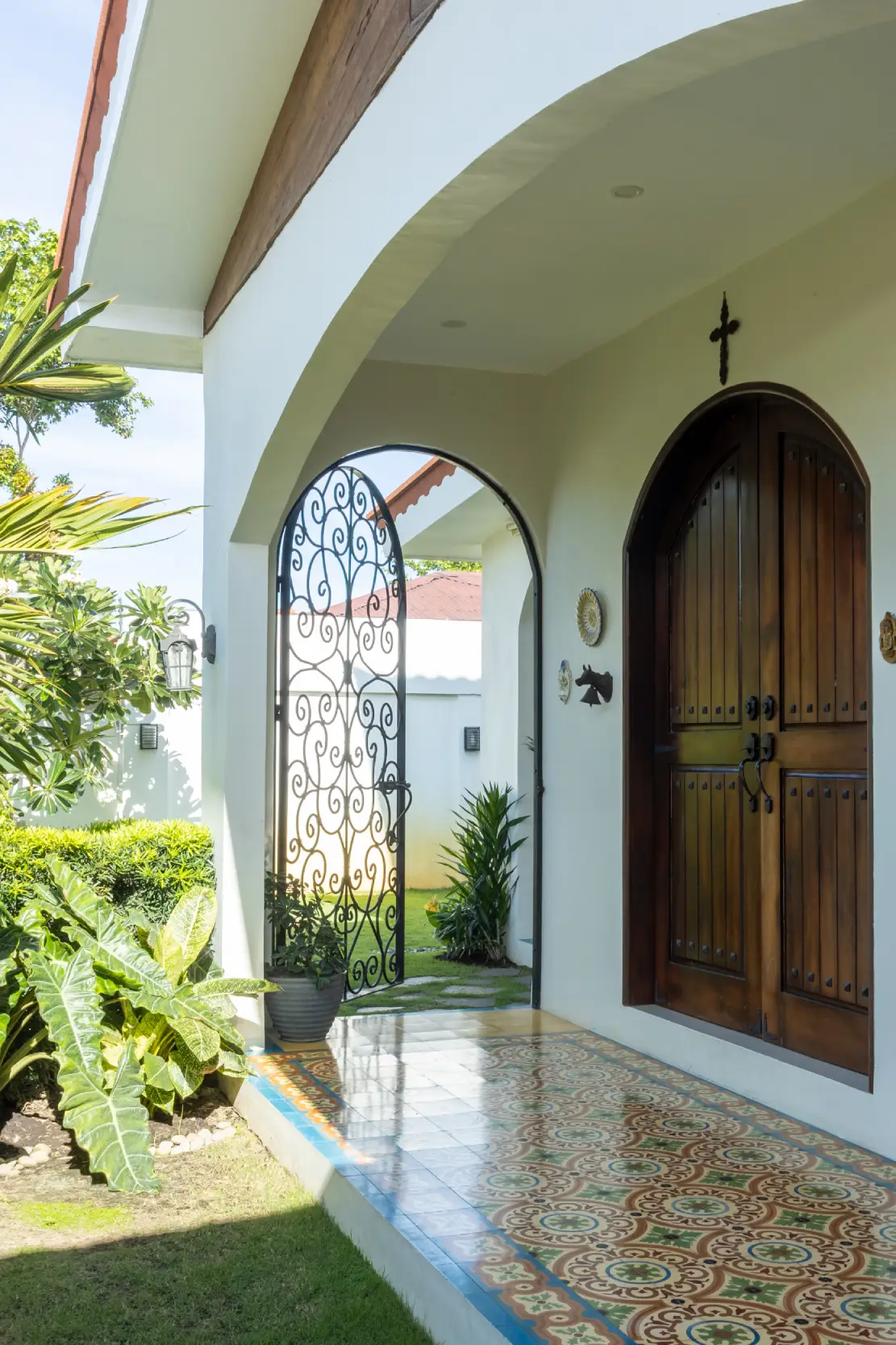 The combination of an arched door, wrought-iron gate, and vibrant Machuca tiles at the porch highlights the Mediterranean character of Casa Mediterranea.