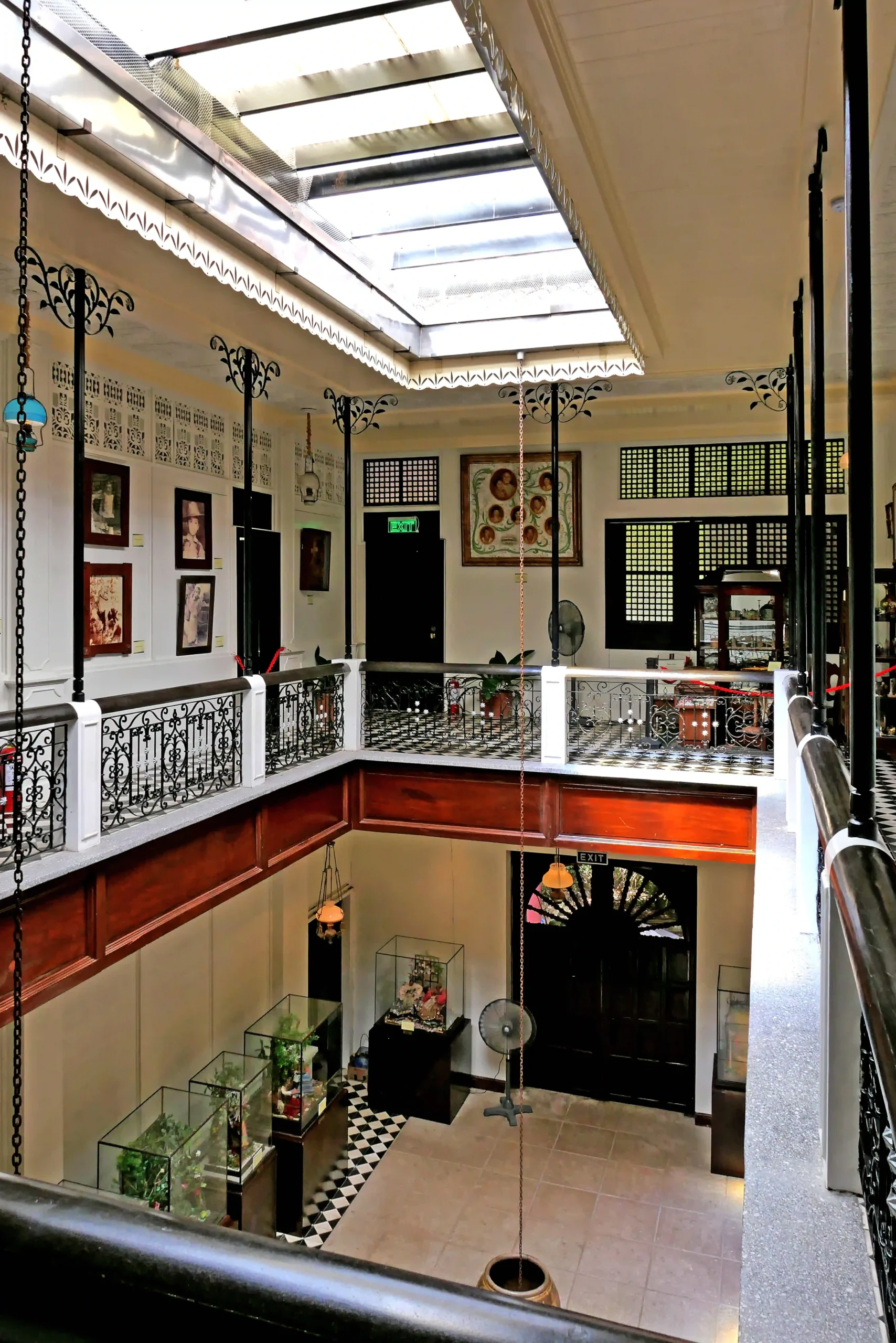 Interior atrium of a historic building with a glass skylight, black decorative railings, and balconies overlooking display cases below.  Villa Escudero Plantation
