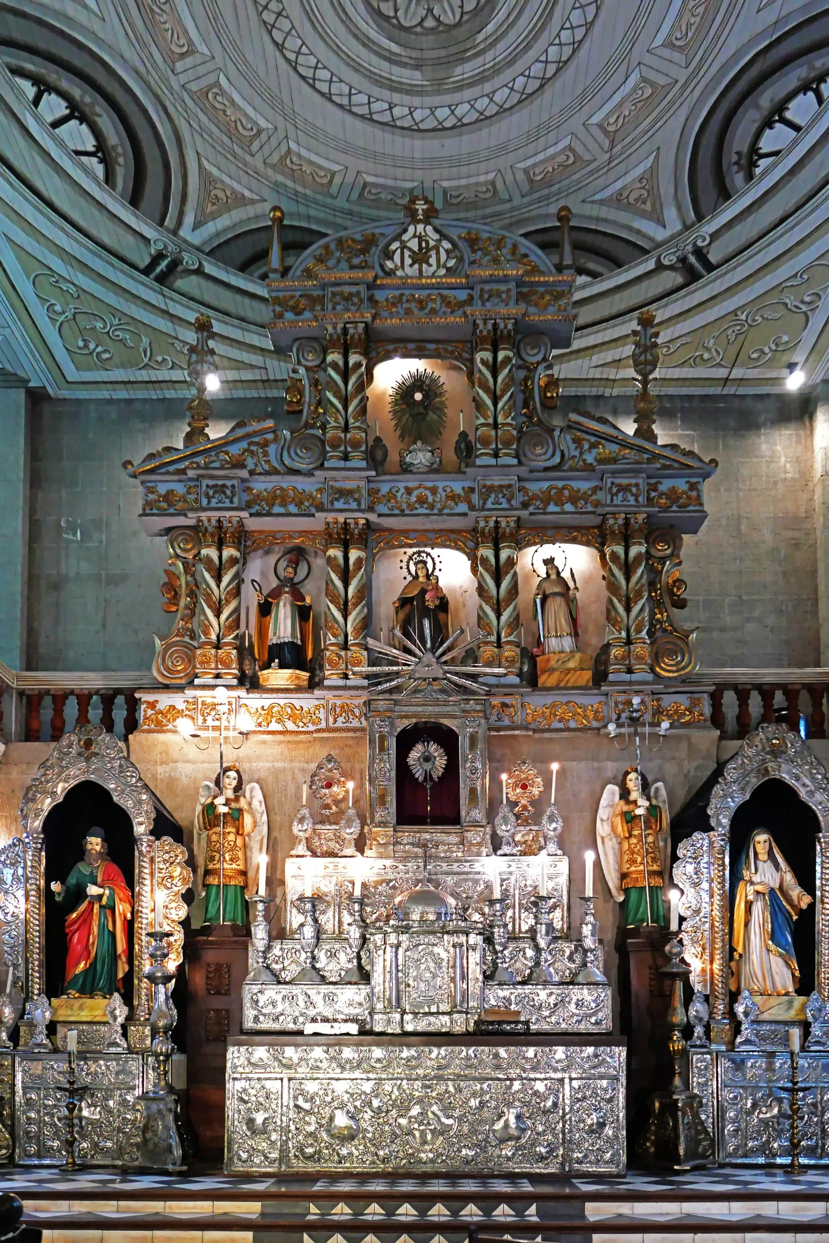 Ornate silver church altar with carved figures and statues beneath a domed, decorative ceiling interior.  Villa Escudero Plantation