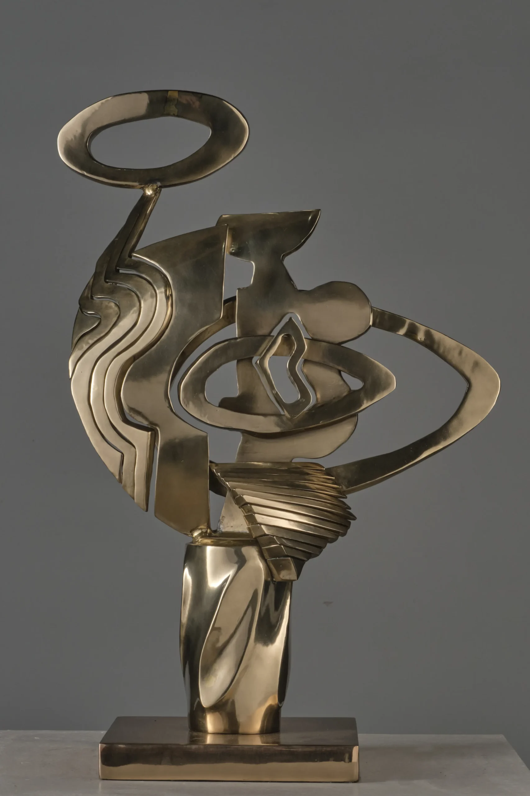 Abstract brass sculpture with intertwined curved shapes and a circular loop on top, mounted on a square pedestal.  Anton V. Quisumbing, Sculpture, Pasulong