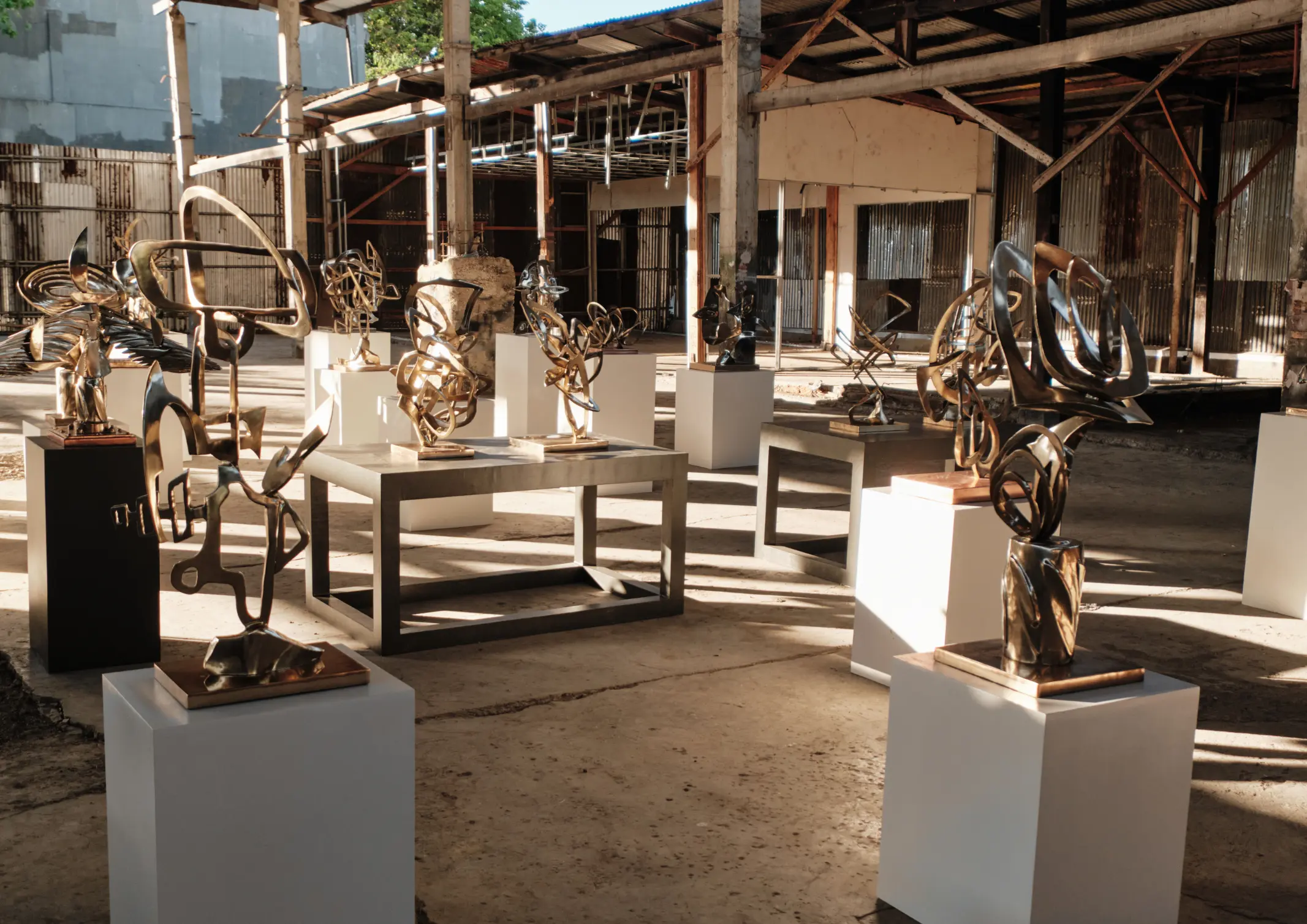 Abstract metal sculptures on white pedestals arranged in an industrial gallery setting.